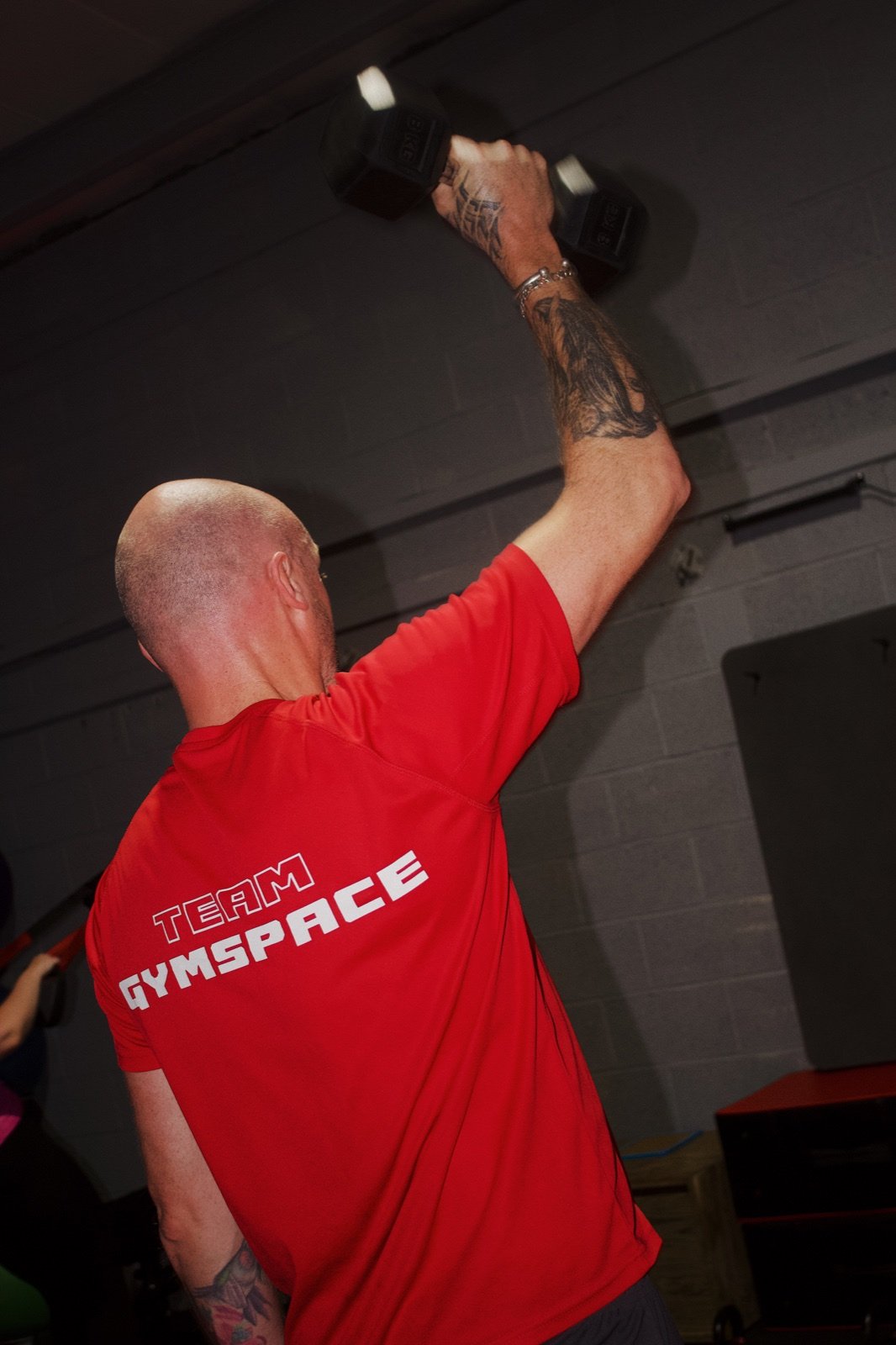 A GymSpace member performing an overhead dumbbell exercise