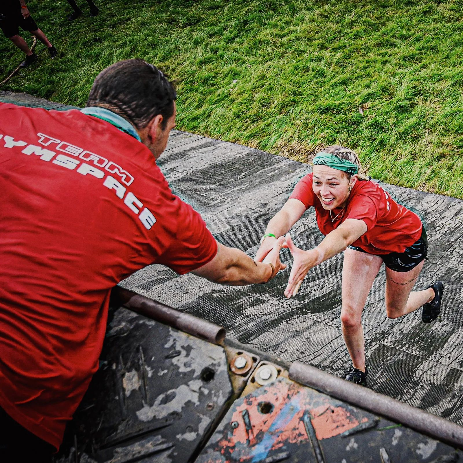A teammate reaching out to help another participant climb an obstacle