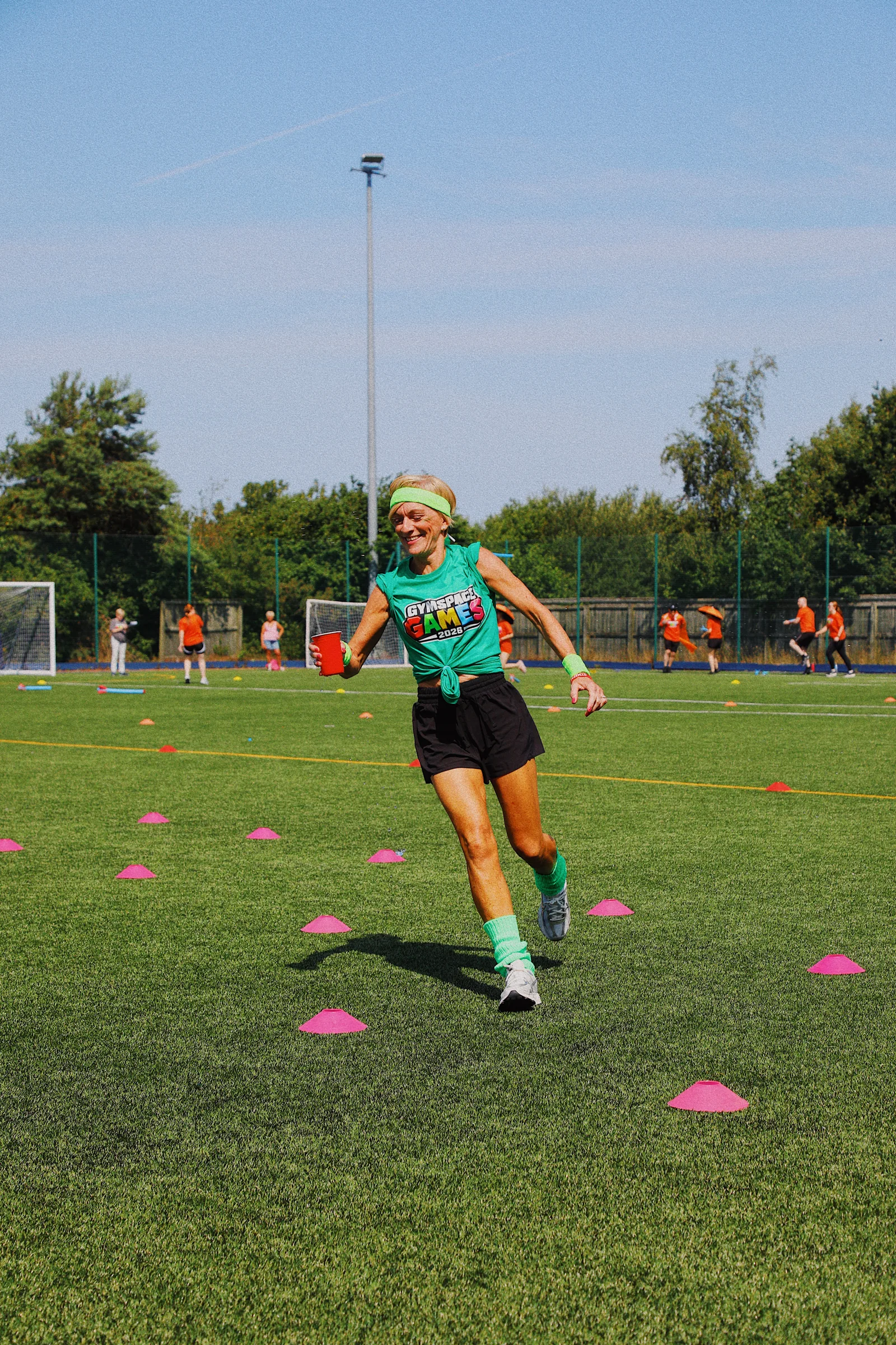 A smiling Green Team participant running with a cup