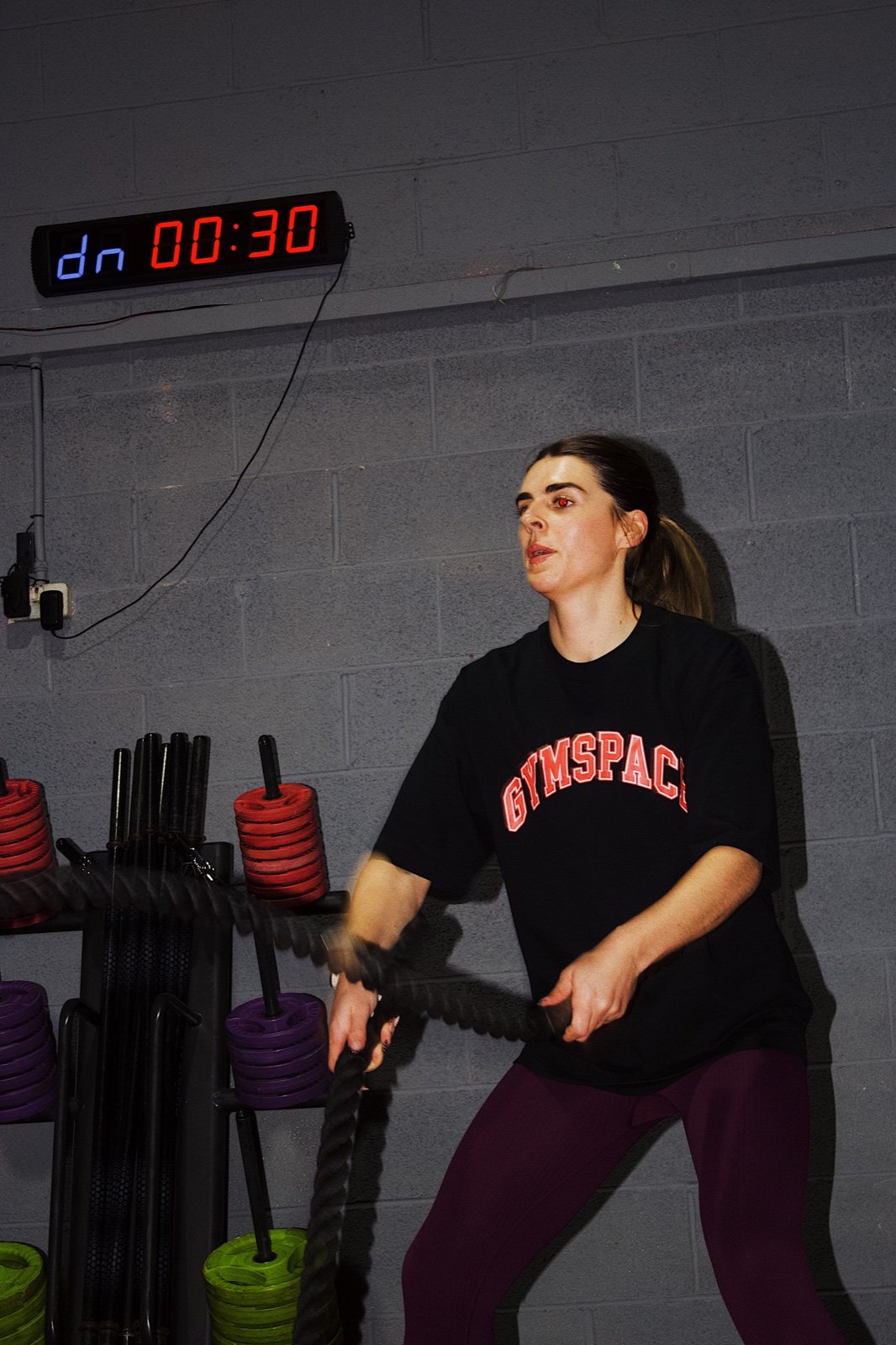 Member wearing a black GymSpace varsity T-shirt while training with battle ropes
