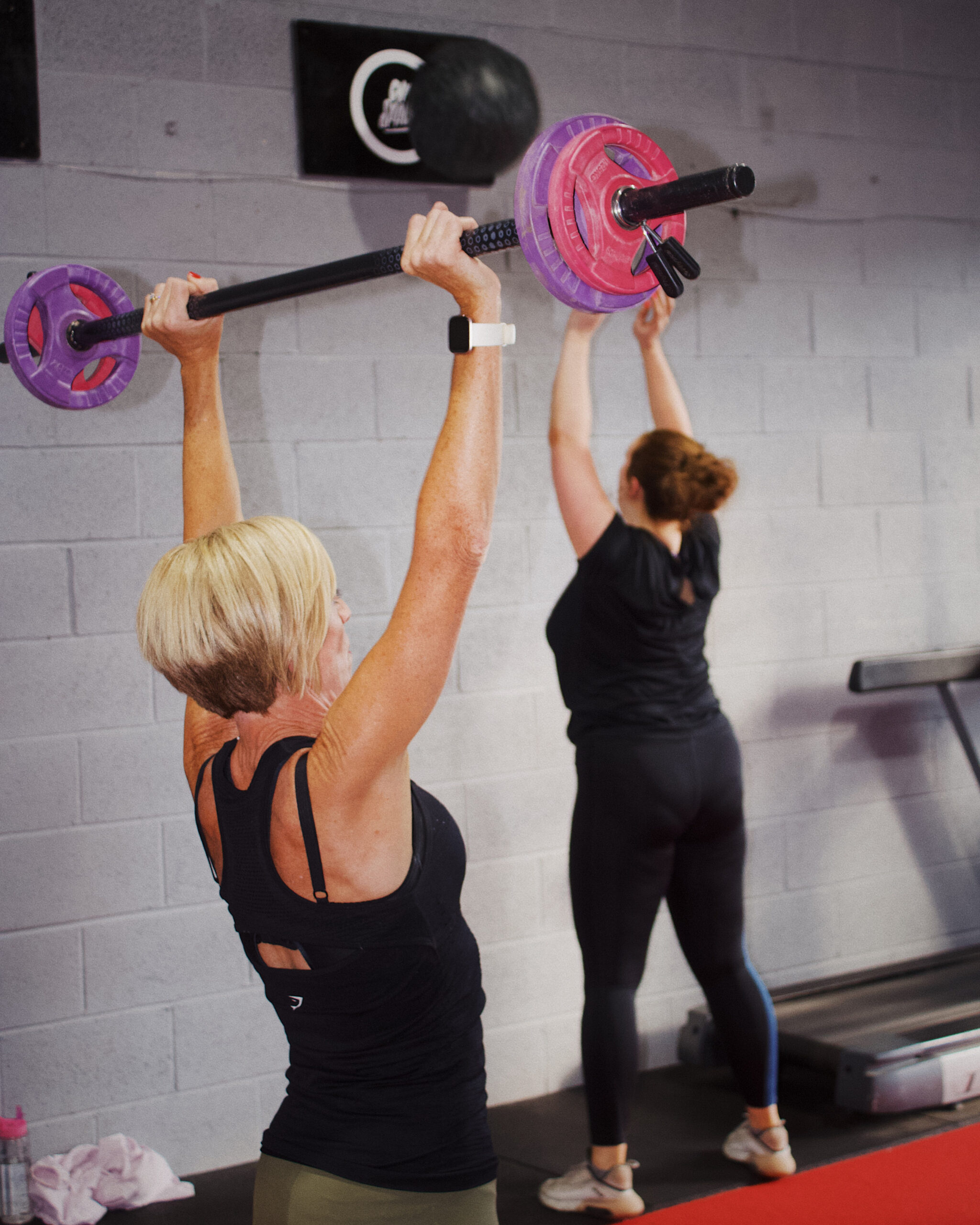 A woman in a HIIT class, determinedly performing a shoulder press with a barbell. This image showcases the strength and focus required in high-intensity interval training.