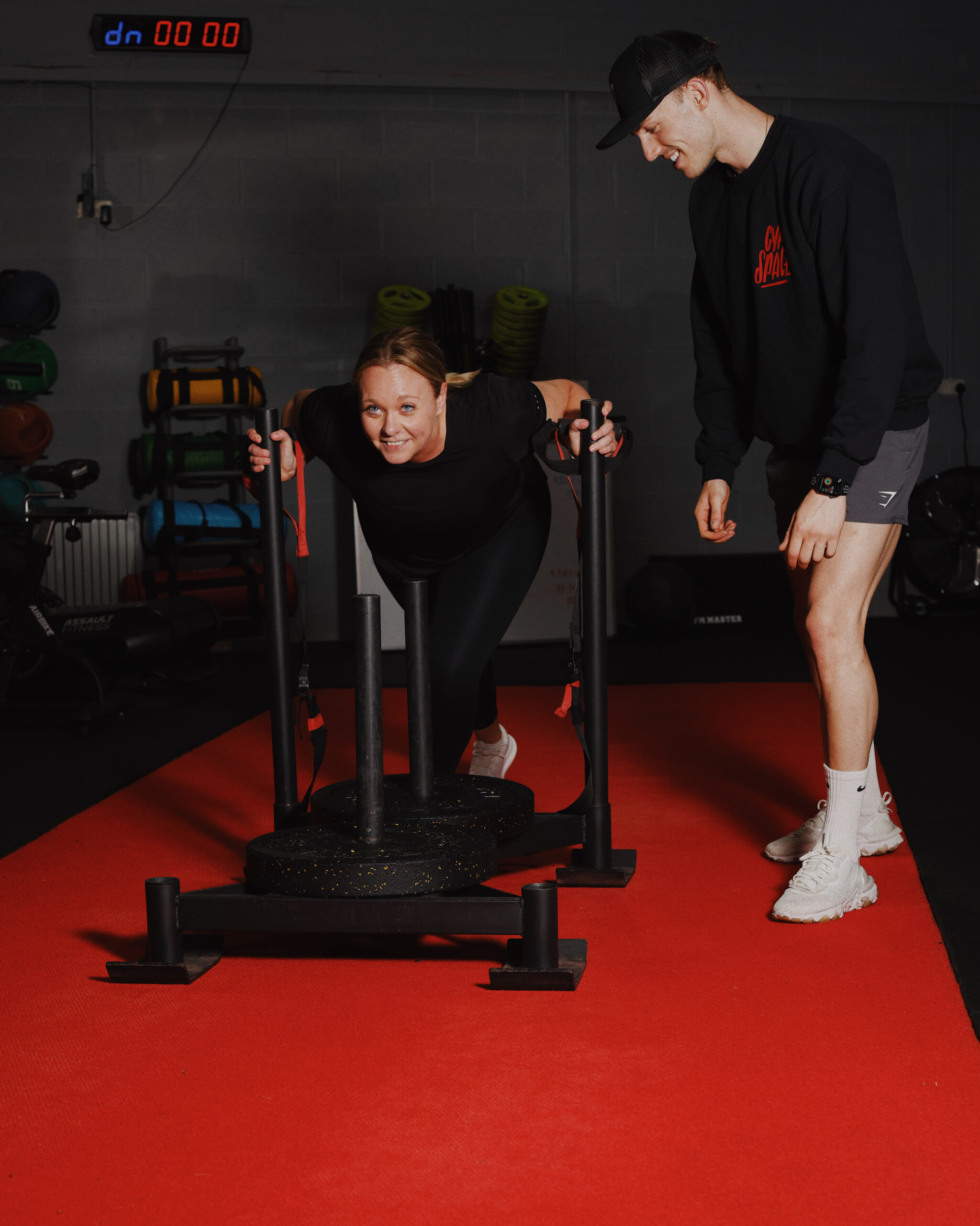 Personal trainer coaching a client during a sled push workout at the gym, focusing on form and technique.